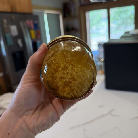A hand holding a glass jar filled with golden honey in a kitchen setting.